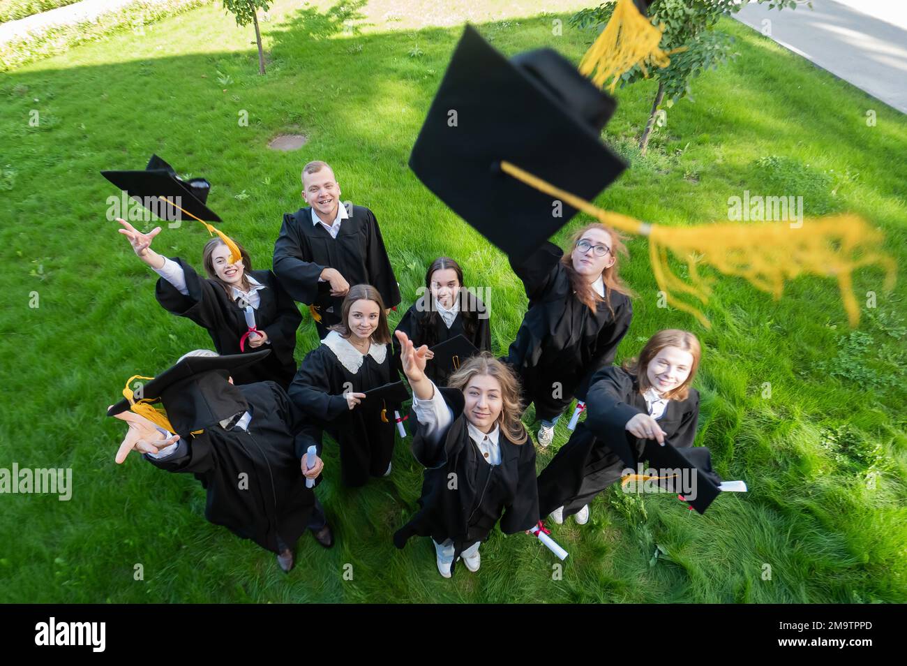 I compagni di classe nei camici di graduazione gettano i loro tappi. Vista dall'alto. Foto Stock