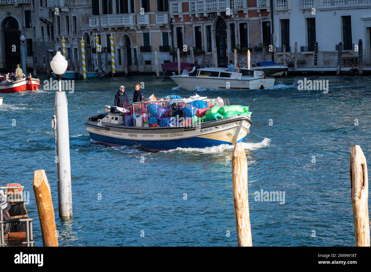 Due uomini guidano una barca piena di spazzatura raccolta dalle strade di Venezia la mattina presto per portarla fuori dalla zona principale della laguna. Foto Stock