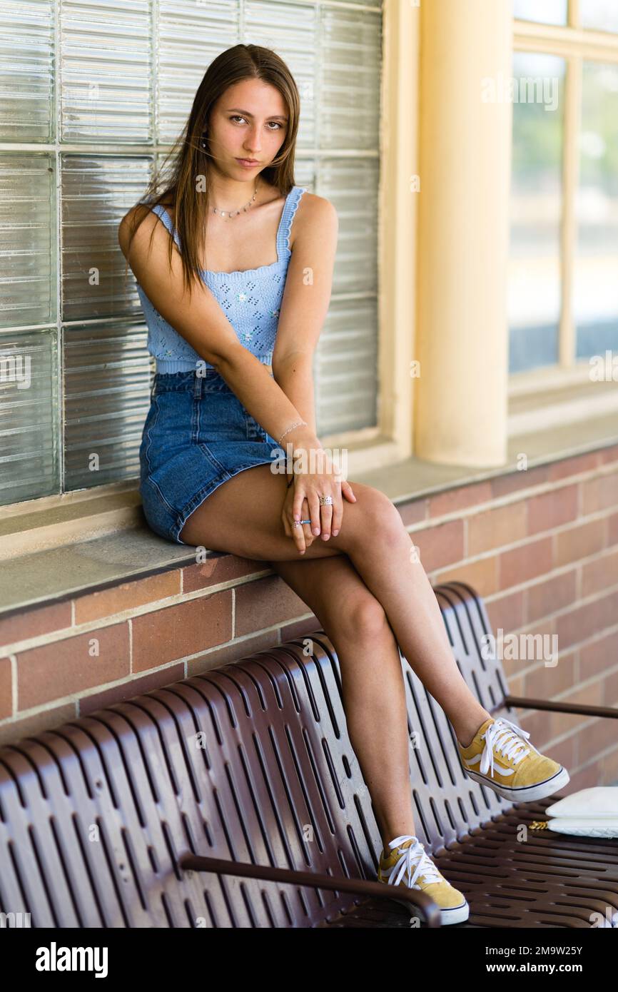 Full Body Portrait di una ragazza teenage alla moda seduta con i piedi sulla panca in una stazione ferroviaria Foto Stock