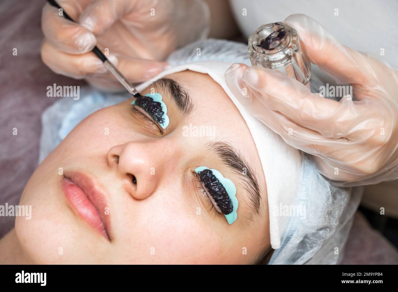 Primo piano ritratto di una donna su procedura di laminazione ciglia. Il maestro applica la tinta alle ciglia. Foto Stock