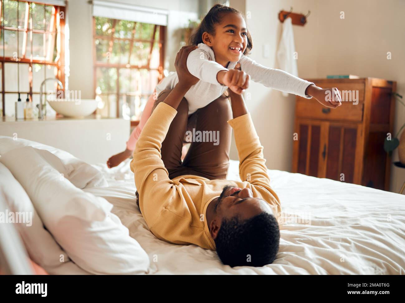 Felice, divertimento e papà con bambino a letto giocando, legame e gioco di aereo per padre e figlia tempo in casa. Famiglia, amore ed energia gioiosa, nero Foto Stock