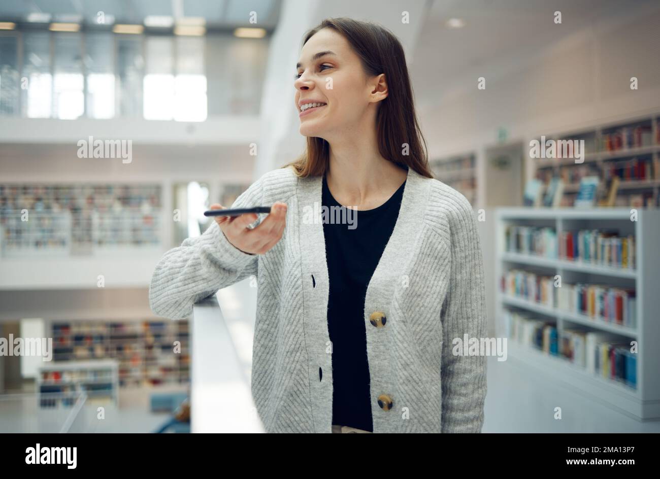 Telefono, biblioteca e donna universitaria in un edificio di istruzione e apprendimento con una conversazione mobile. Libri, studenti e conversazione di ricerca di un college Foto Stock