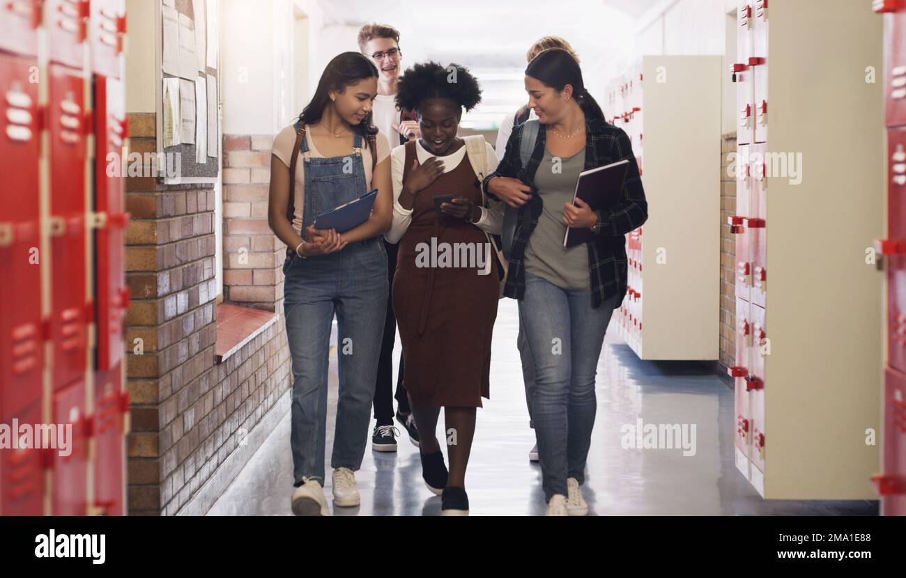Una buona istruzione può arrivare lontano. un gruppo di adolescenti che camminano lungo la hall e utilizzano uno smartphone al liceo. Foto Stock