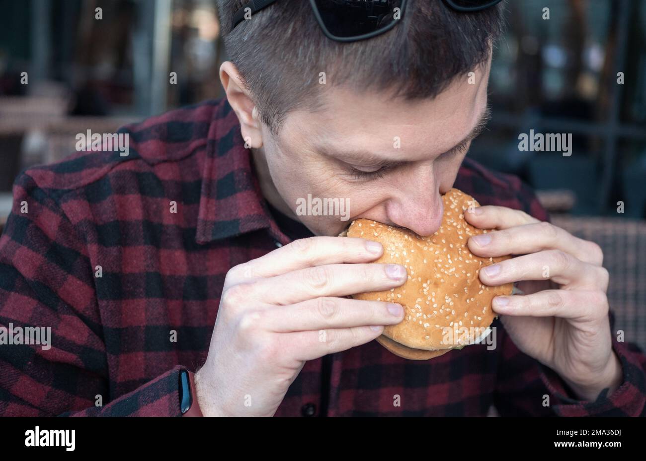 Ritratto di un uomo affamato che mangia hamburger nel caffè della città. Foto Stock