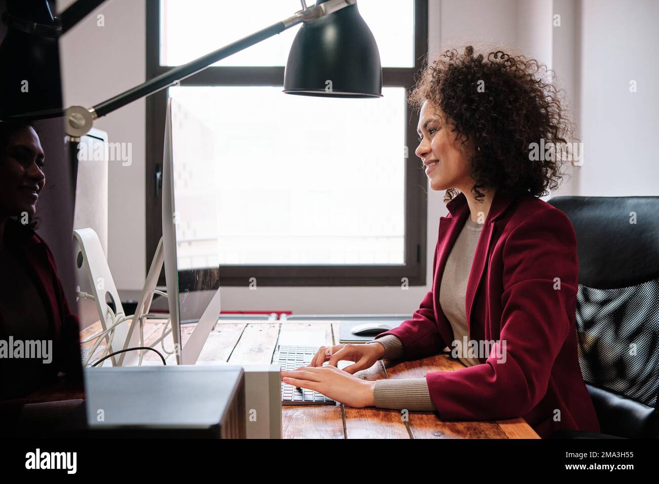 Donna sorridente mentre lavora con il computer in ufficio. Foto Stock