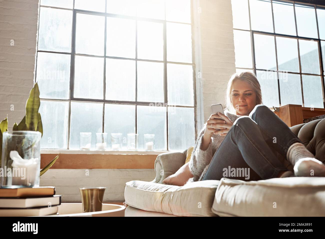 Donna con smartphone, social media e relax, comunicazione e tecnologia mentre si rilassa sul divano a casa. Telefono, digitazione online e connettività Foto Stock