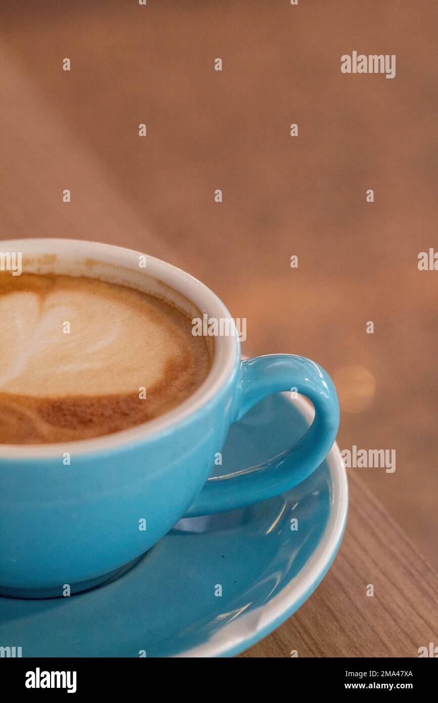 Caffè con latte in una grande tazza blu con un mini croissant mentre si telelavoro in una caffetteria ad Alicante con lo sfondo fuori fuoco. Foto Stock