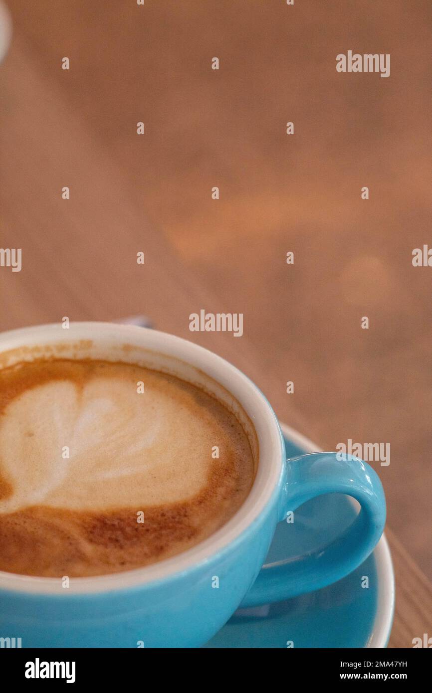 Caffè con latte in una grande tazza blu con un mini croissant mentre si telelavoro in una caffetteria ad Alicante con lo sfondo fuori fuoco. Foto Stock