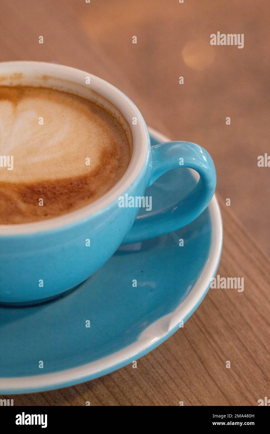 Caffè con latte in una grande tazza blu con un mini croissant mentre si telelavoro in una caffetteria ad Alicante con lo sfondo fuori fuoco. Foto Stock