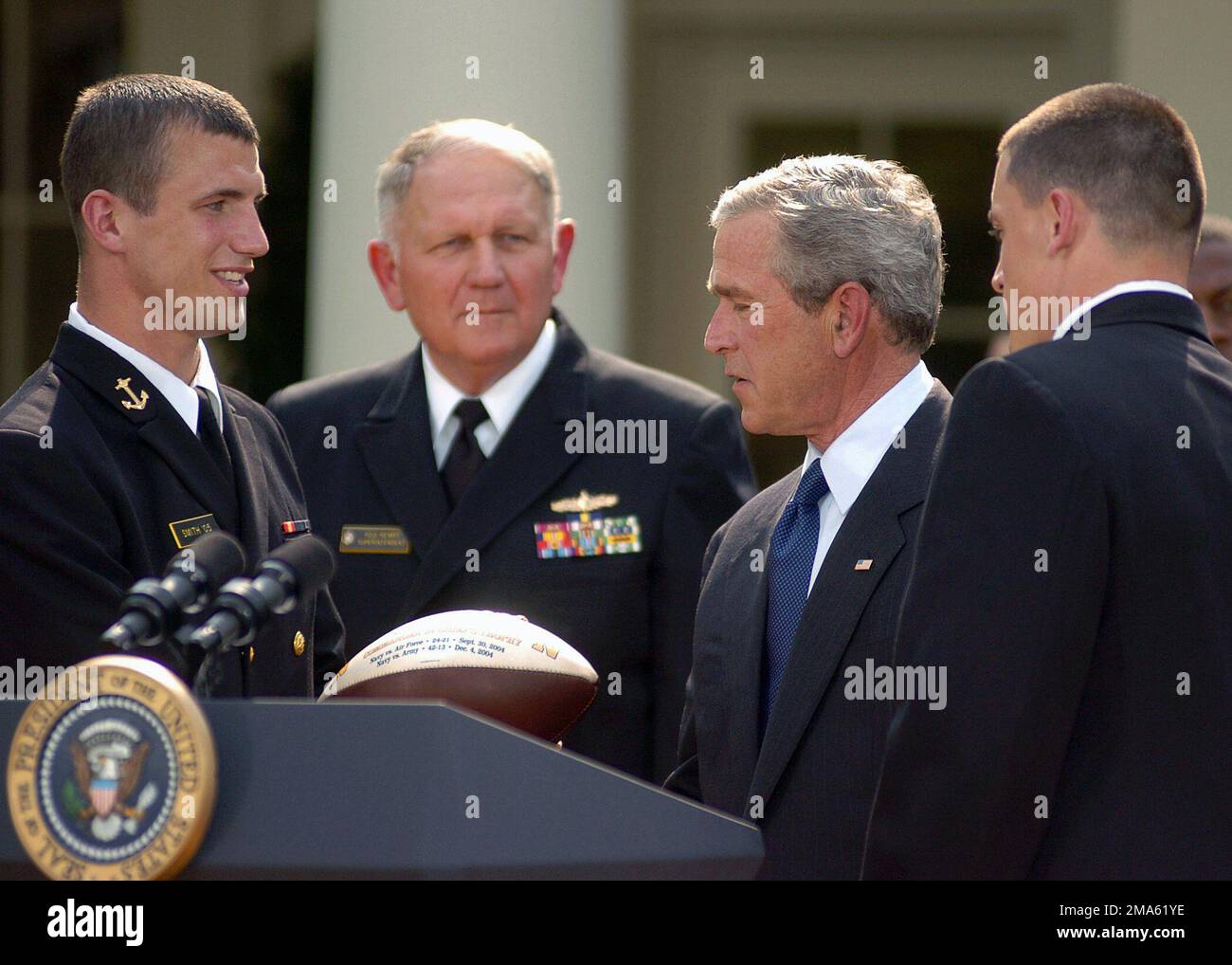 050420-N-0000A-002. [Complete] Scene Caption: US Navy Academy (USNA) Midshipman First Class (MIDN 1/C) Josh Smith (a sinistra), presenta un calcio al presidente americano George W. Bush durante la presentazione del Trofeo Comandante-in-CHIEF ai membri della squadra di calcio USNA in una cerimonia al White House Rose Garden. Dietro MIDN 1/C Smith c'è l'ammiraglio USN Vice (VADM) Rodney P. Rempt, sovrintendente dell'Accademia Navale degli Stati Uniti, e a destra del presidente è MIDN 1/C Aaron Polanco, team Quarterback. Il presidente Bush si è congratulato con il team per aver vinto il trofeo del comandante in CAPO per il secondo anno consecutivo. Foto Stock