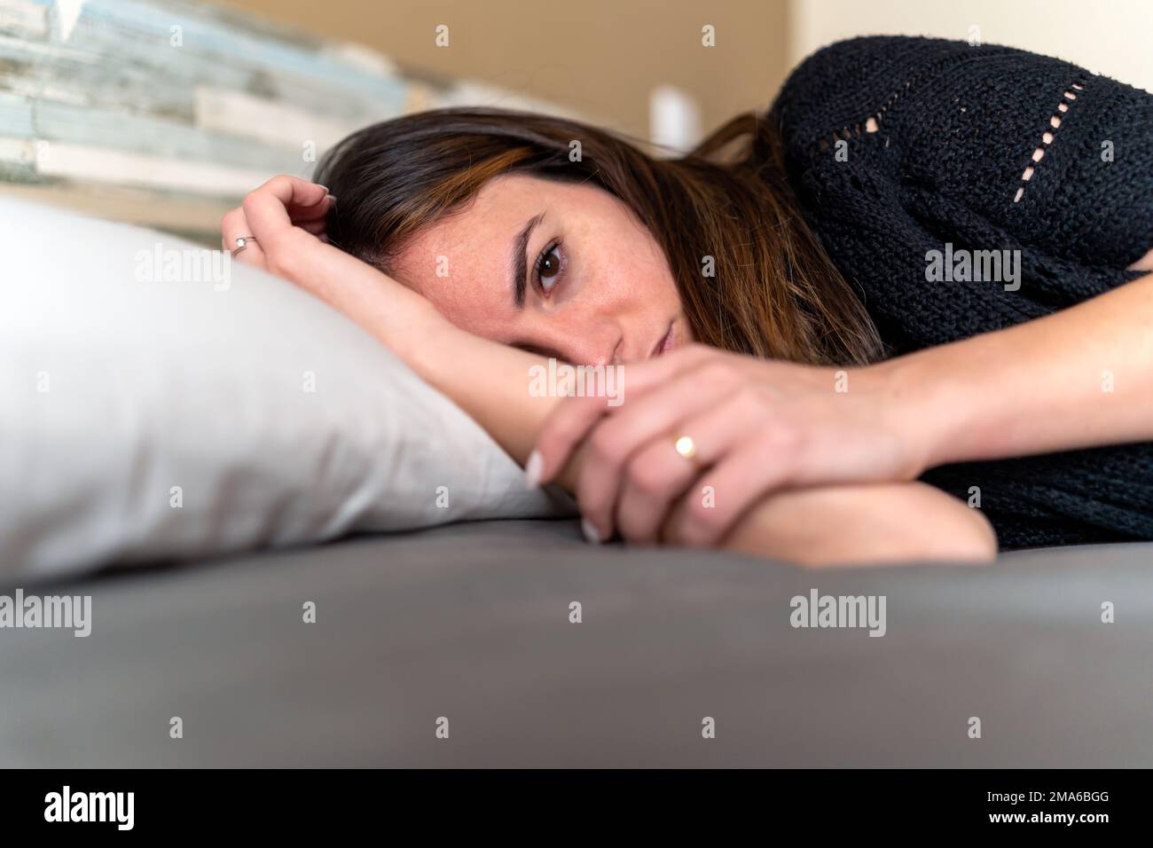 vista laterale di una giovane bruna trista sdraiata a letto, con problemi mentali malata di depressione Foto Stock