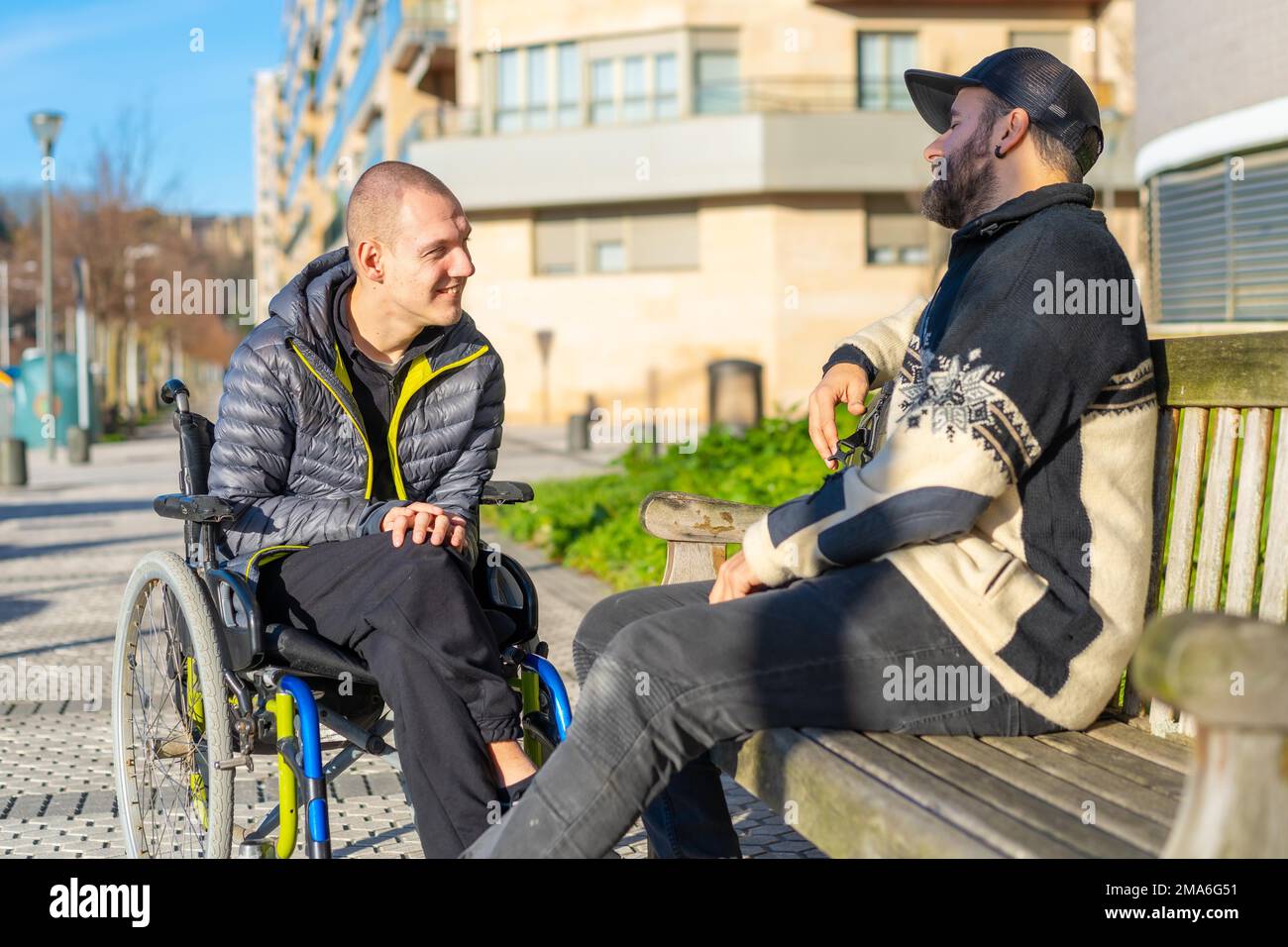 Una persona disabile su una sedia a rotelle con un amico seduto a divertirsi, normalità per i disabili Foto Stock