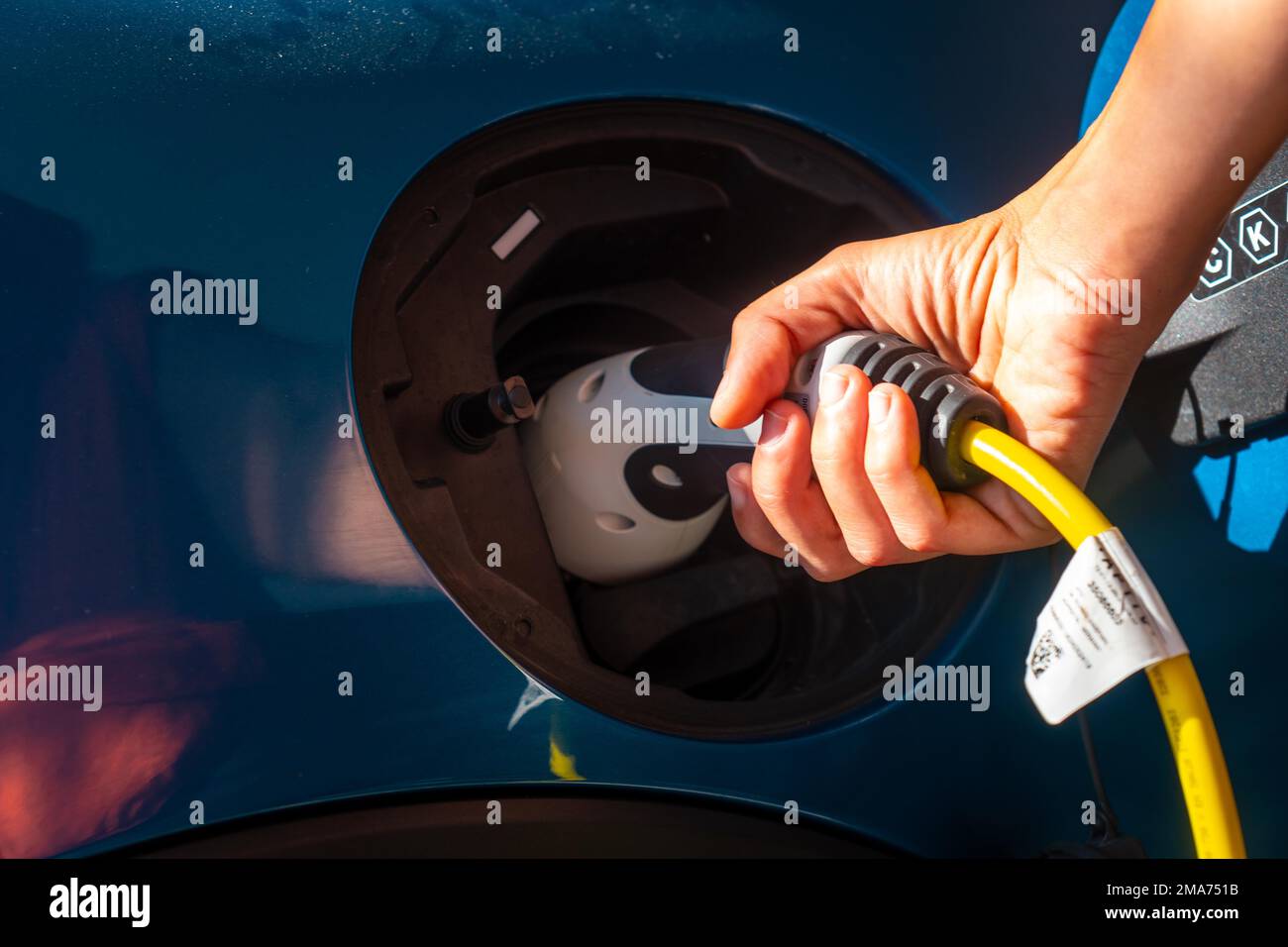 Particolare di una mano che tiene un'auto elettrica che carica le batterie nel garage della casa, non benzina Foto Stock