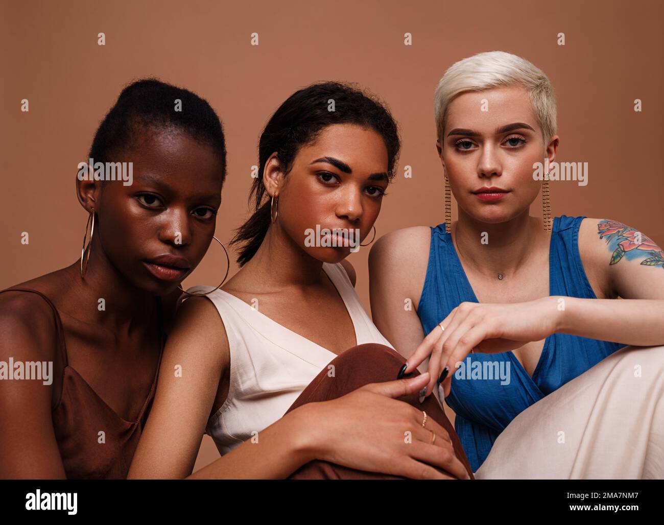 Tre donne in abiti seduti insieme su sfondo marrone Foto Stock