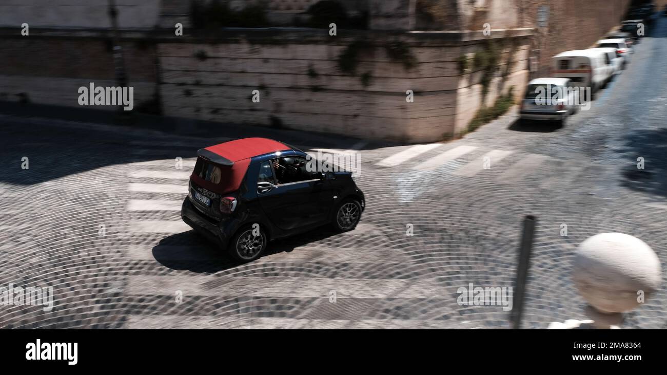 Un'auto intelligente che viaggia sulle strade acciottolate di Roma, passando sopra una strada pedonale. Foto Stock