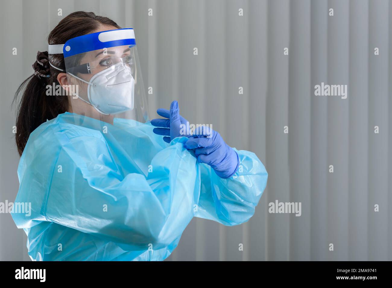 L'infermiera sta indossando i guanti protettivi mentre indossa la maschera N95 con la visiera protettiva sul viso Foto Stock