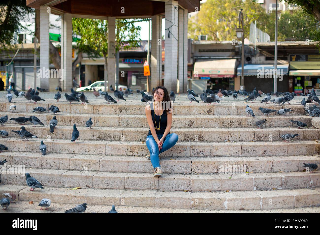 Una bella ragazza è seduta sui gradini del parco circondato da piccioni. Foto Stock