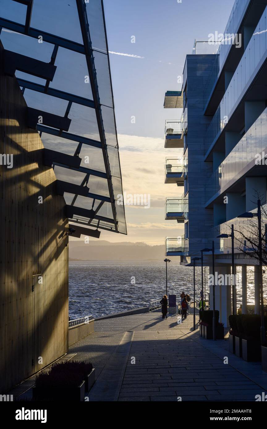 Vista lungo Tjuvholmen Allé a Aker Brygge tra edifici moderni in controluce contrastic verso Oslofjord in bassa luce solare autunnale. Oslo, Norvegia. Foto Stock
