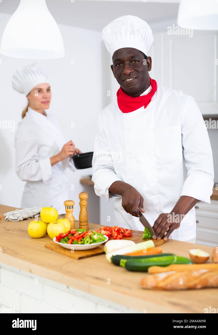 Chef professionista in uniforme bianca che lavora con assistente femminile in cucina privata Foto Stock