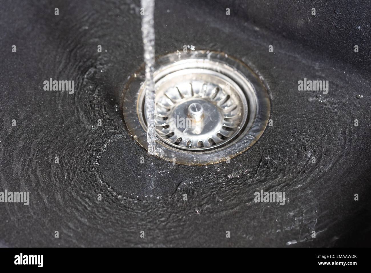 L'acqua che cade dal rubinetto al lavello inossidabile e fluisce verso il foro dell'acqua, concetto di bevanda Foto Stock