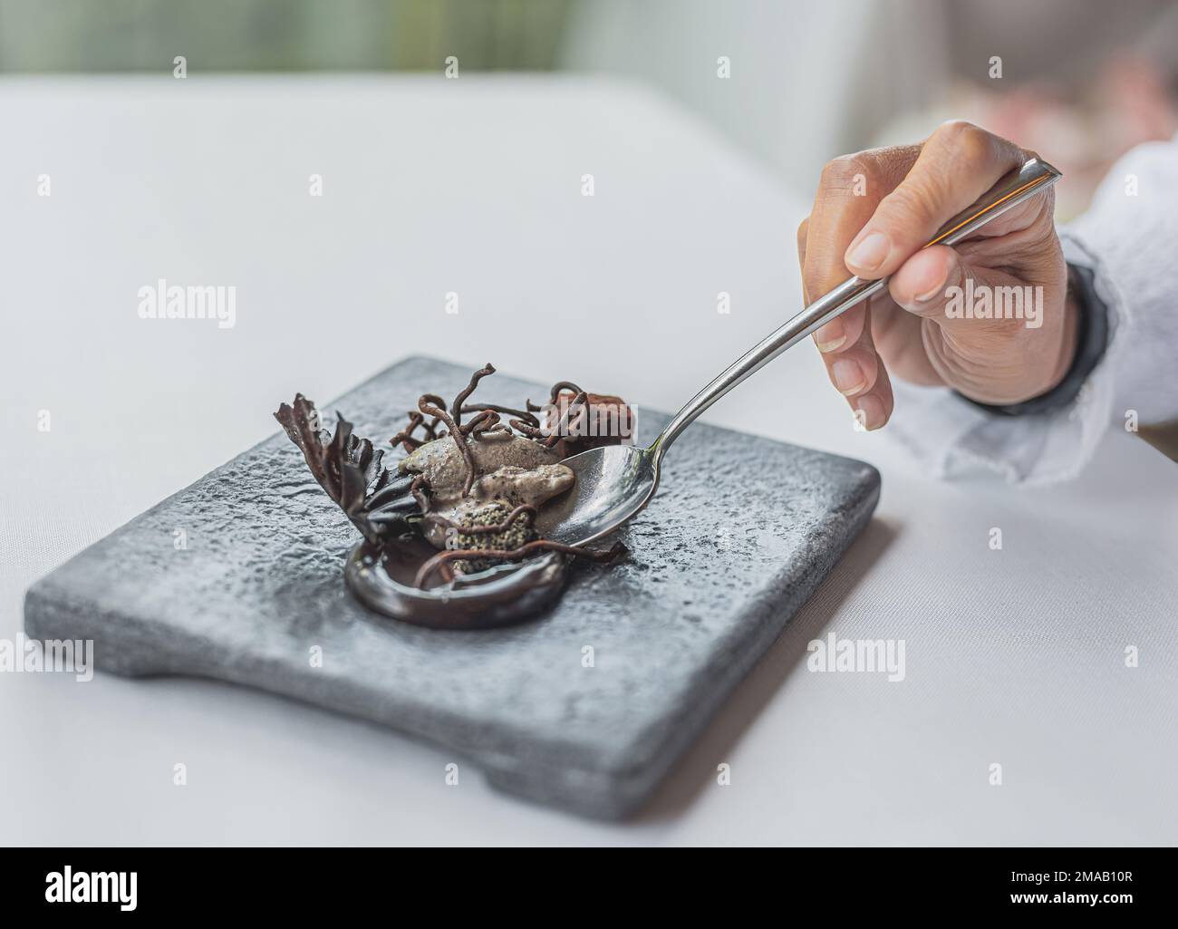 un dettaglio di una persona che assaggia un dessert di alta cucina. dettaglio della mano e del cucchiaio. il dessert è cacao e oliva nera. Foto Stock