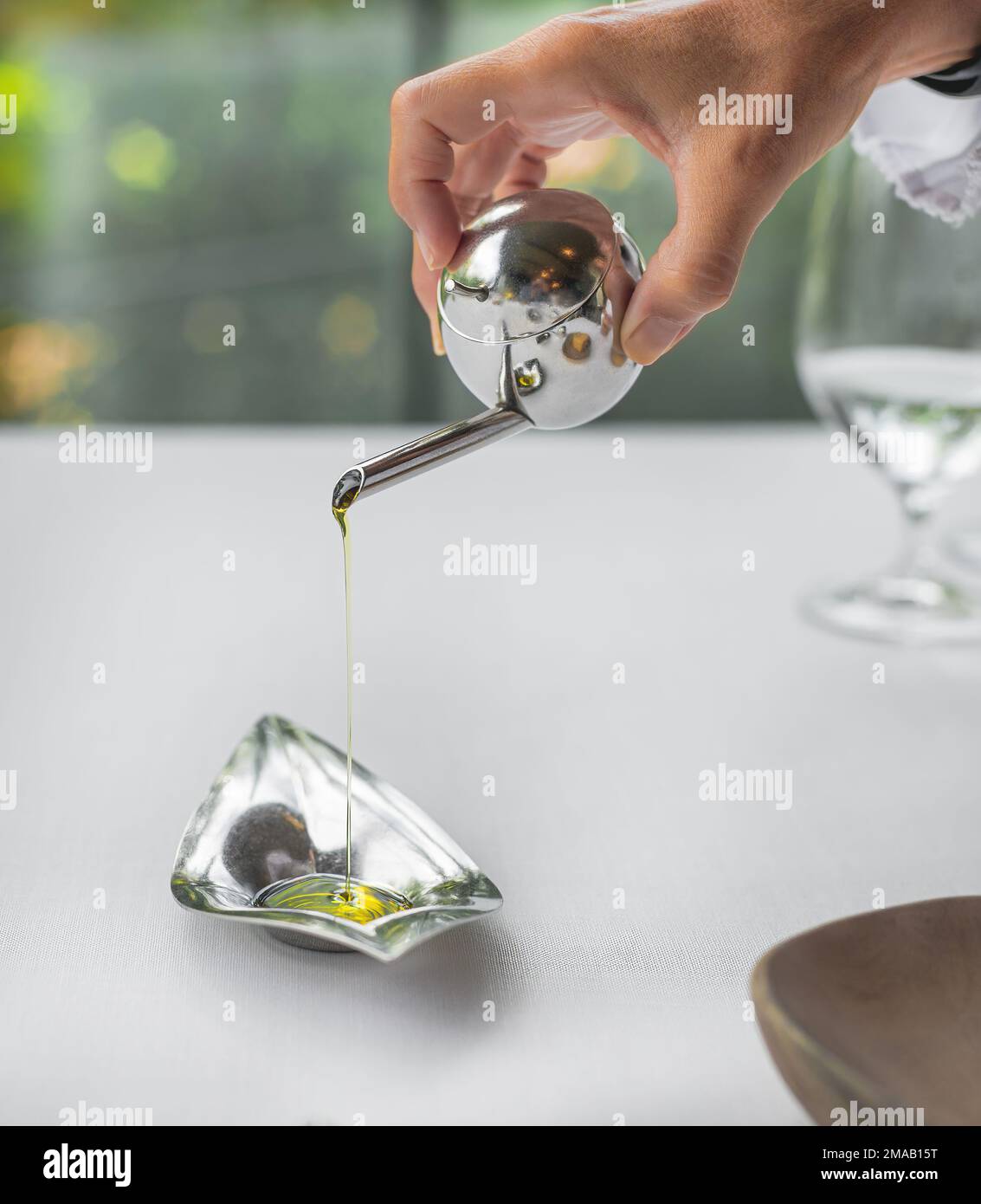 particolare di una persona che versa olio d'oliva su una ciotola di metallo. concetto di alta cucina e prodotti gourmet. prodotti mediterranei. cibo sano. Foto Stock