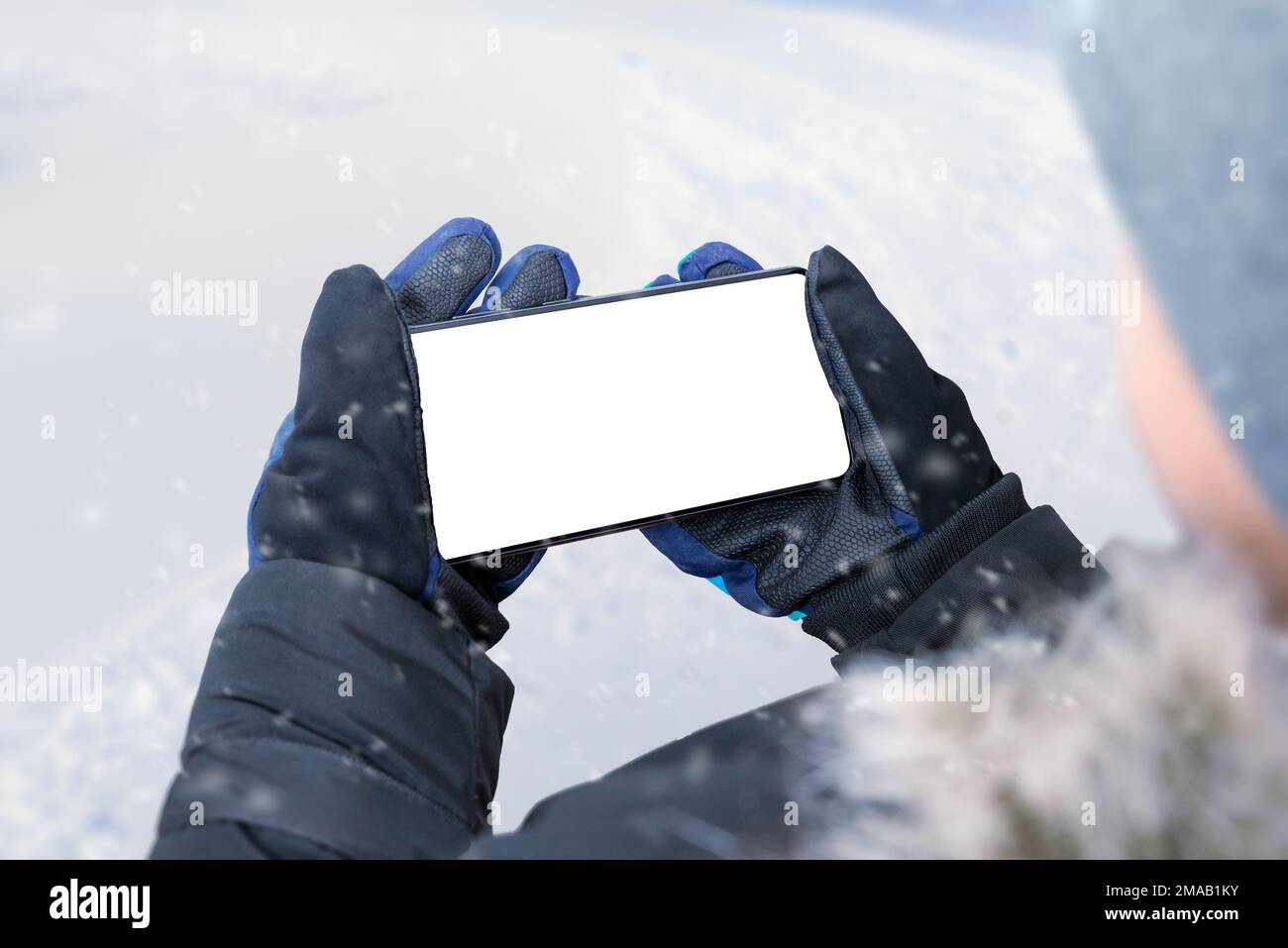 Telefono nelle mani del ragazzo in posizione orizzontale. Ragazzo in giacca invernale, guanti e berretto. Display isolato per il mockup. Inverno Foto Stock
