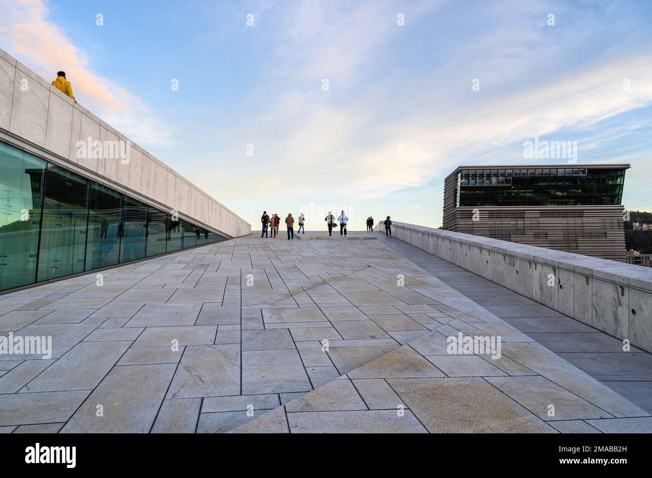 I visitatori che camminano su una delle numerose superfici accessibili del tetto spiovente del Teatro dell'Opera di Oslo. Museo Munch sulla destra. Oslo, Norvegia. Architetti Snøhetta. Foto Stock