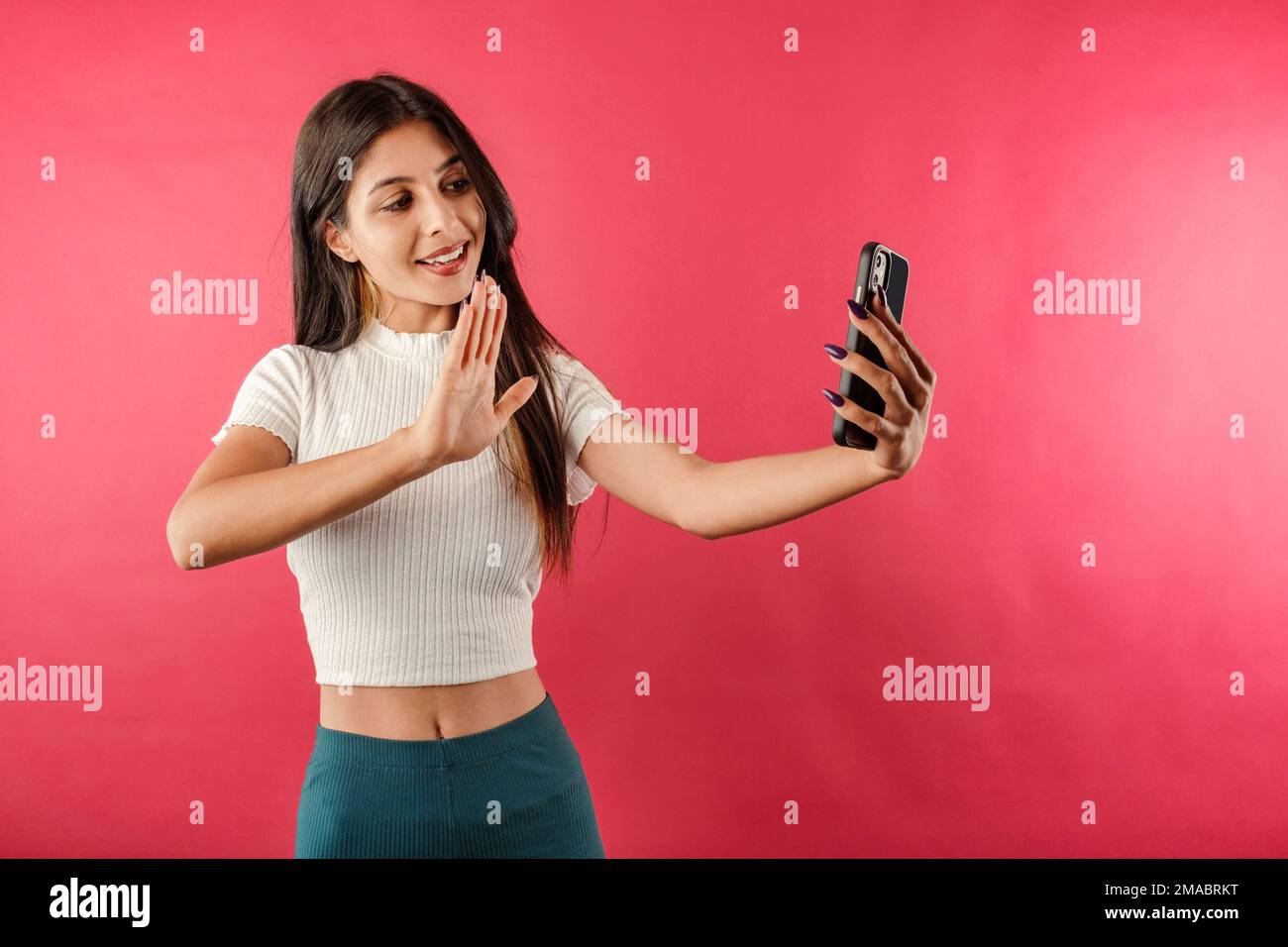 Giovane donna bellissima che indossa un taglio a coste isolato su sfondo rosso utilizzando lo smartphone per le videochiamate. Chat video, conversazione sul telefono cellulare tramite v Foto Stock