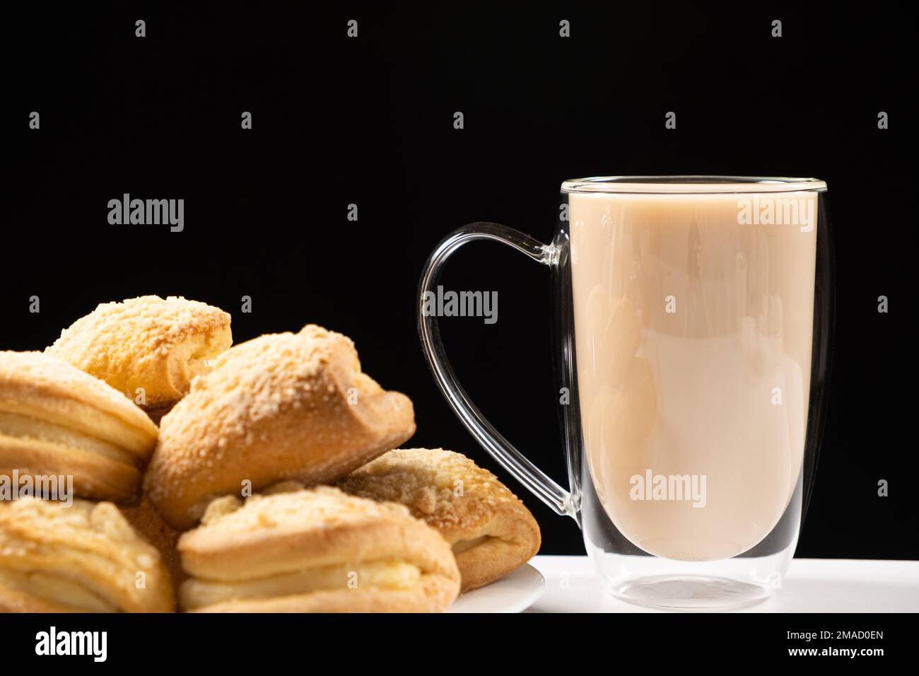 Tè con latte in una tazza di vetro con doppio fondo e torte su sfondo nero Foto Stock