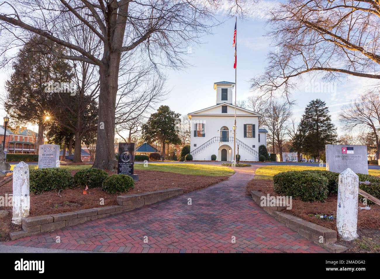 DALLAS, NC, USA-5 GENNAIO 2023: Ingresso principale allo storico edificio e ai terreni della Gaston County Court House del 1848. Passaggio pedonale in mattoni, palo della bandiera, monumento Foto Stock