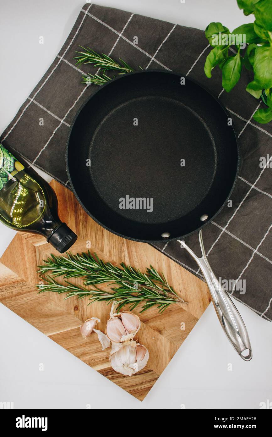 padella nera su fondo bianco con un asse di legno con aglio. giacitura piatta Foto Stock