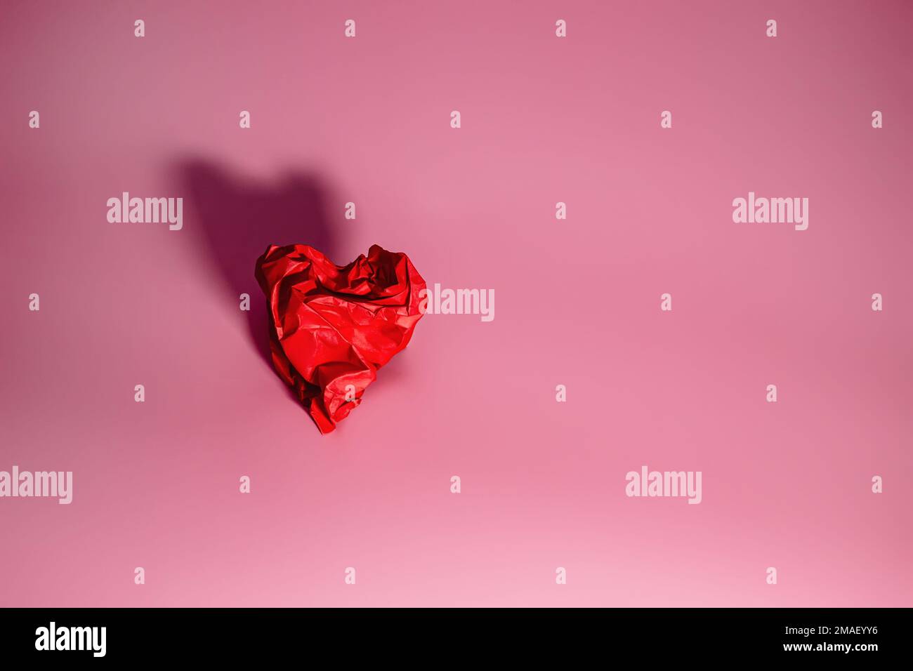 Cuore rosso di carta rumpled su uno sfondo rosa con ombra. Concetto di San Valentino. Un simbolo di separazione, tristezza Foto Stock