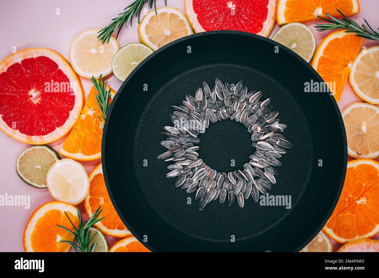 padella nera con semi di girasole, da cui si crea un fiore di girasole sulle piante di agrumi tagliate a fette. Arance, pompelmo, limone, lime Foto Stock