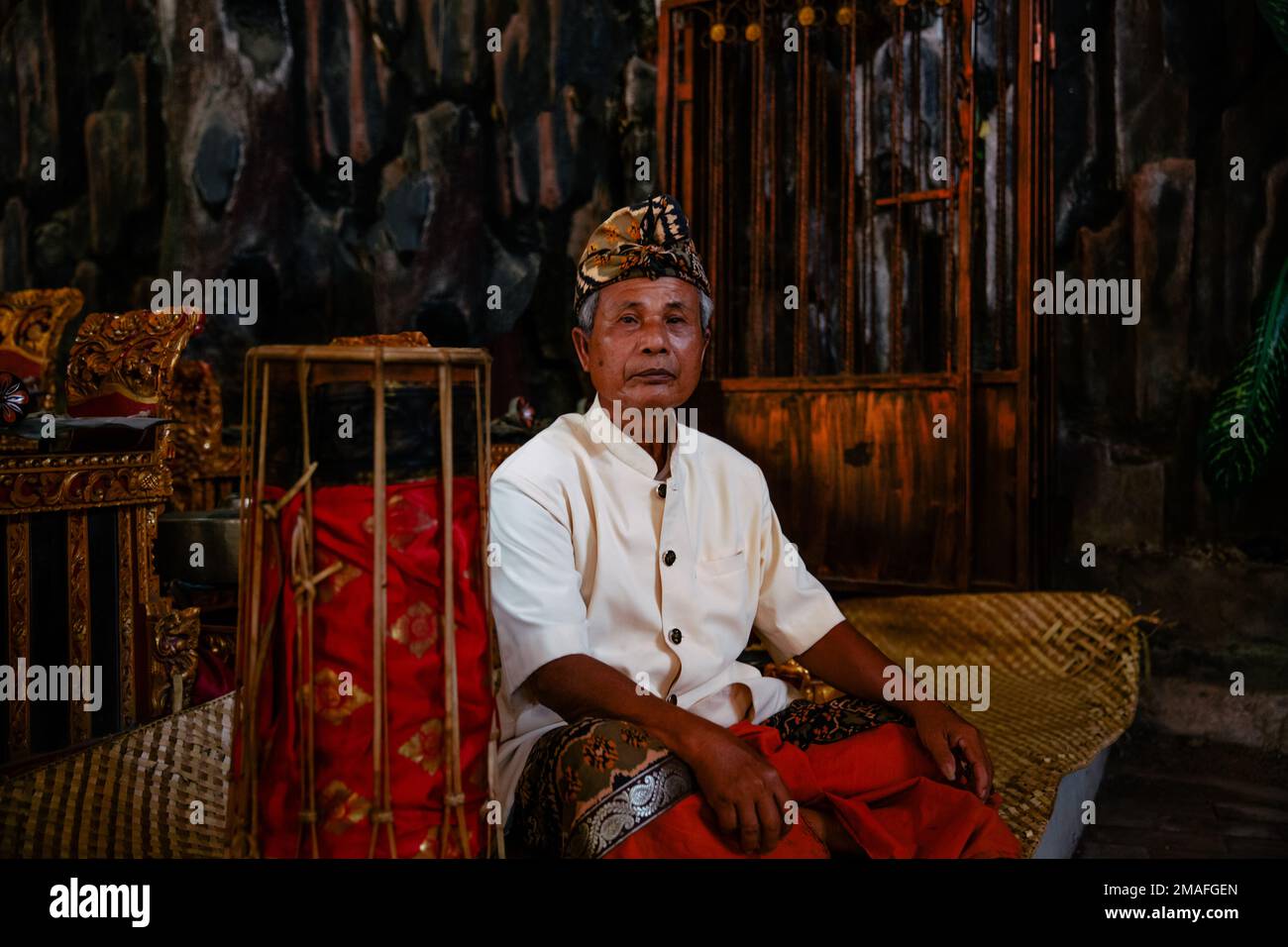 Bali - Indonesia - 10.22.2015: Anziano musicista indonesiano vestito con abiti tradizionali seduto da solo con una faccia diritta Foto Stock