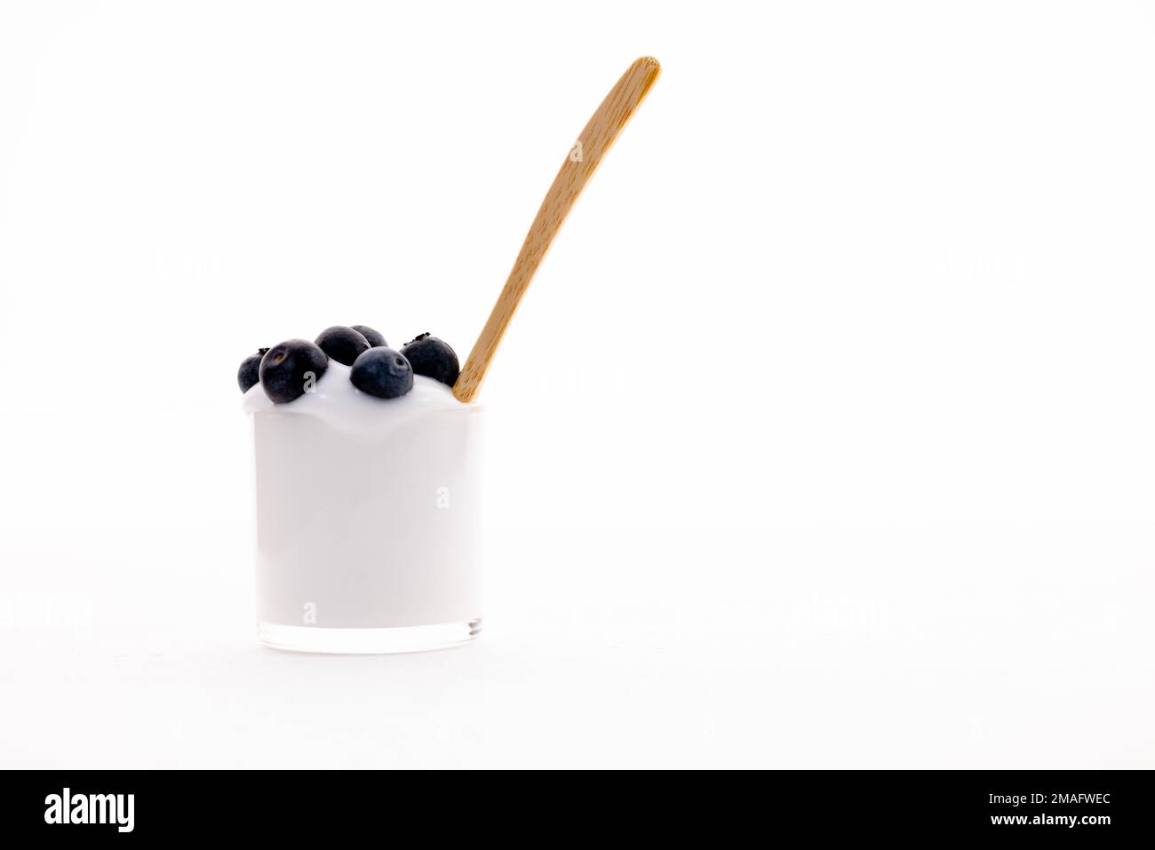 Yogurt greco biologico isolato con mirtilli e cucchiaio di legno su fondo bianco intenso Foto Stock