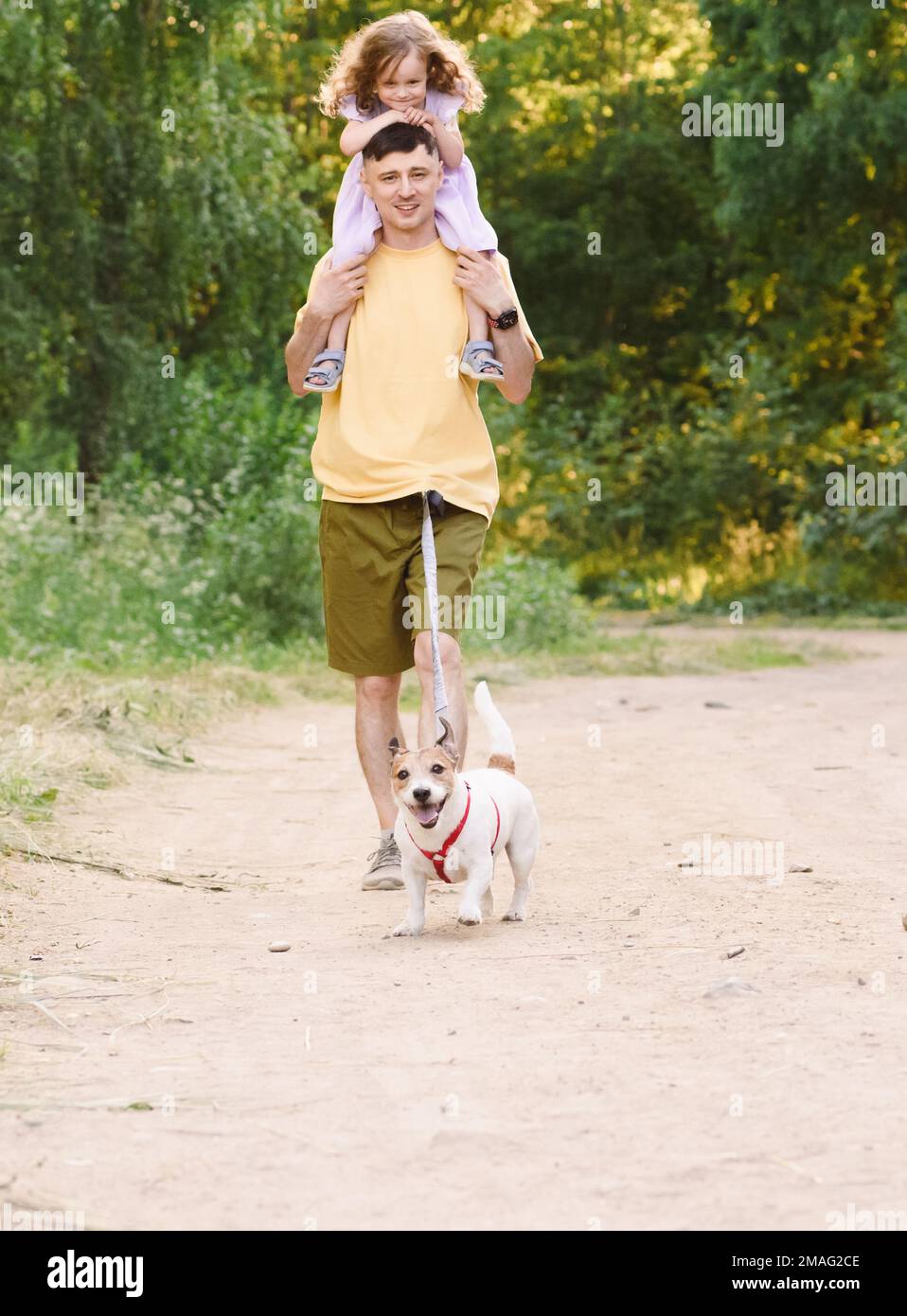 Padre e figlia che camminano fuori dalla strada sterrata di campagna con cane da compagnia sul guinzaglio in vita Foto Stock