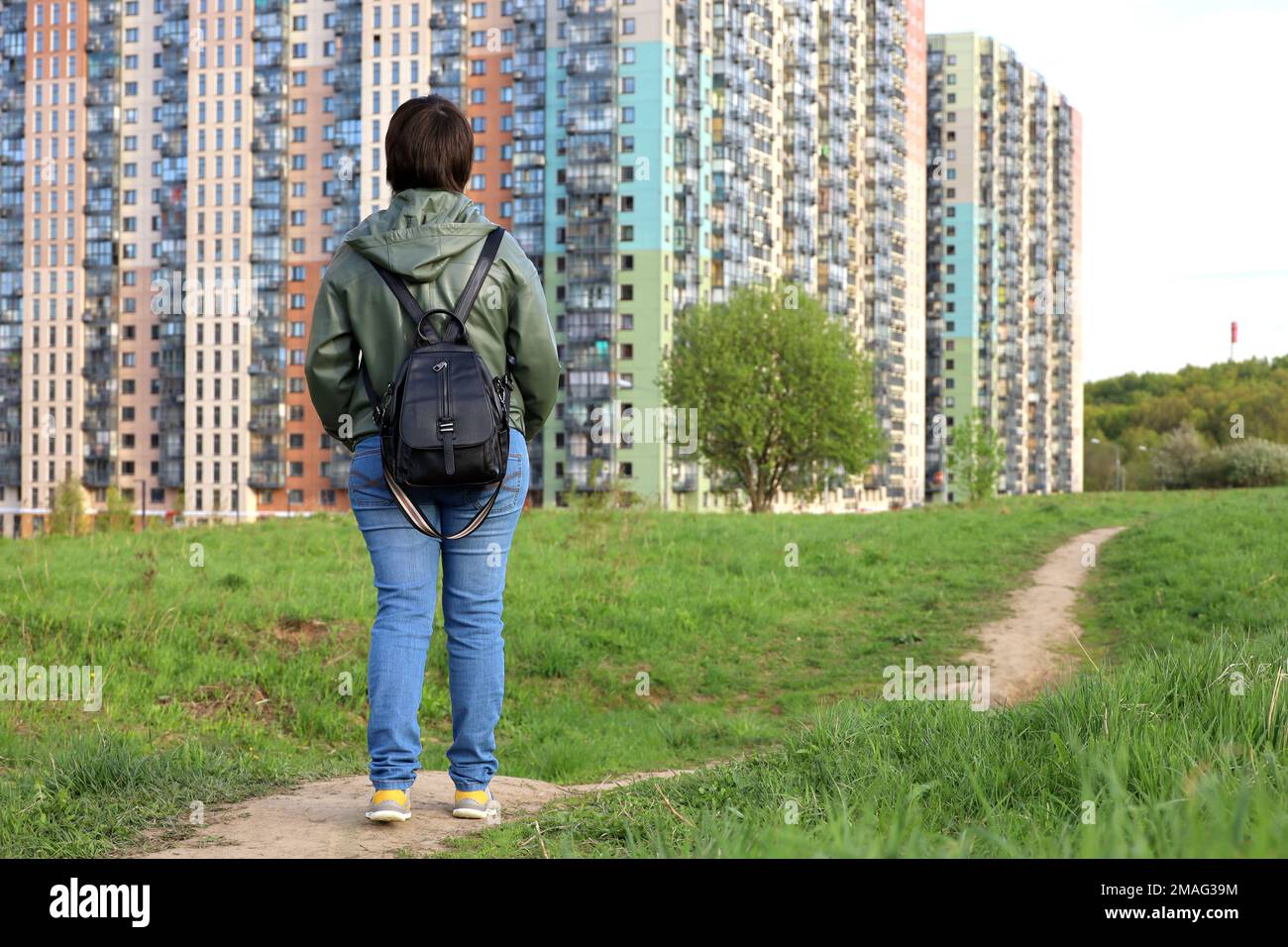 Donna su prato verde guarda i nuovi edifici, quartiere residenziale in zona ecologicamente pulita. Settore edilizio e concetto immobiliare Foto Stock