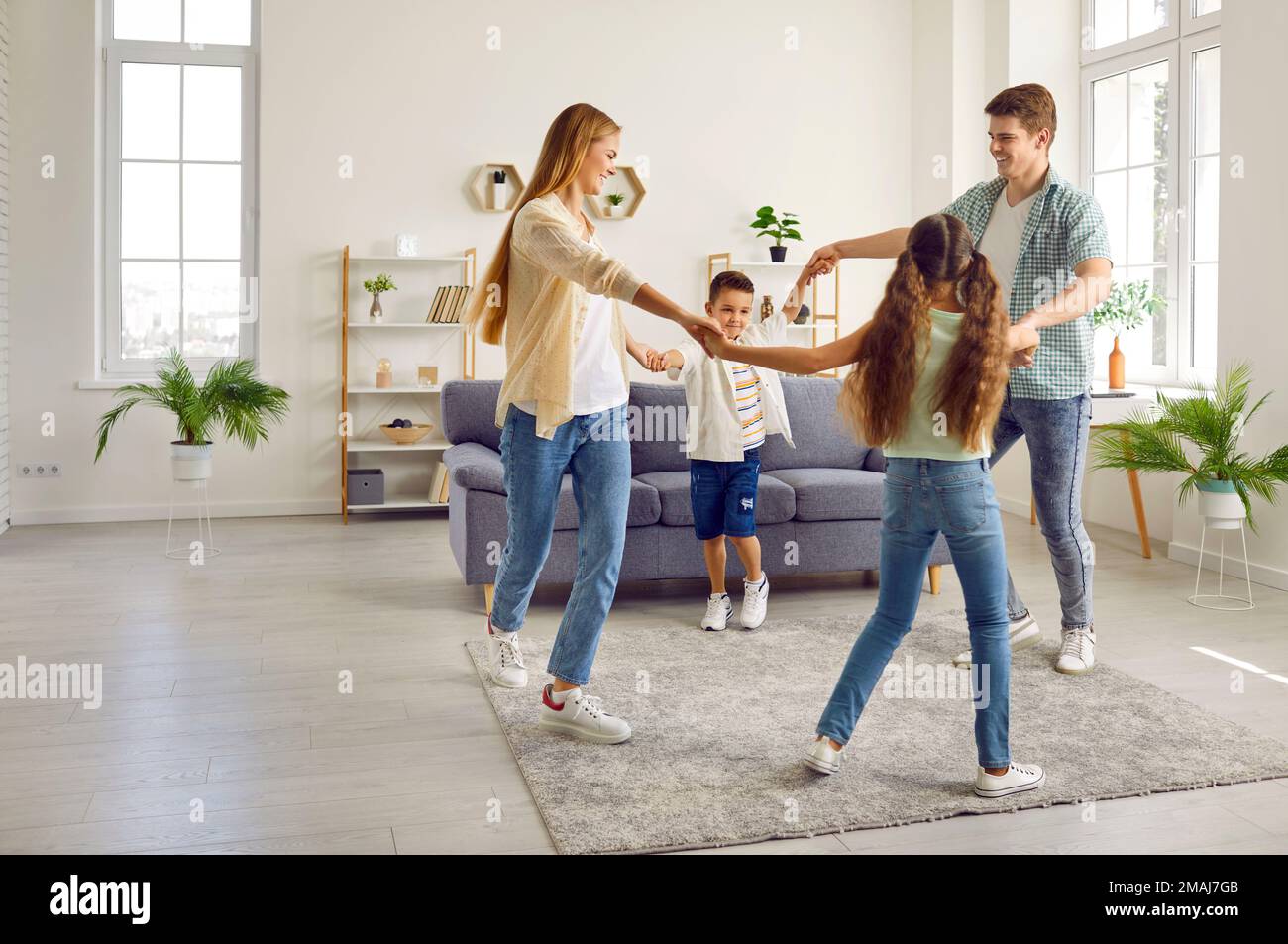 Una famiglia felice con due bambini sta giocando a condurre una danza rotonda a casa nel soggiorno. Foto Stock