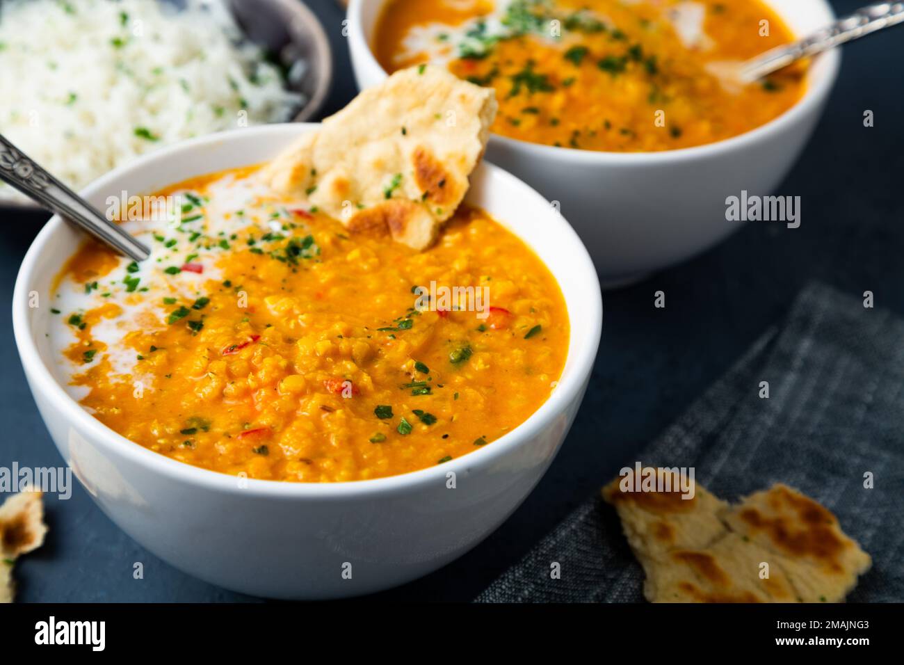 Zuppa di lenticchie rosse con latte di cocco e curry accompagnati da riso basmati e pane naan su sfondo blu scuro Foto Stock