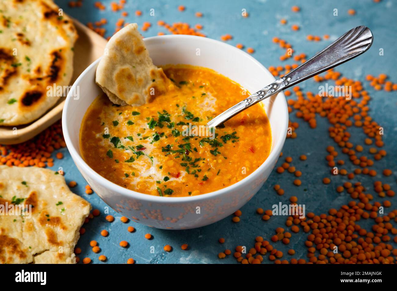 Zuppa di lenticchie rosse con latte di cocco e curry accompagnata da pane naan sorrotondo da lenticchie non cotte su sfondo blu Foto Stock