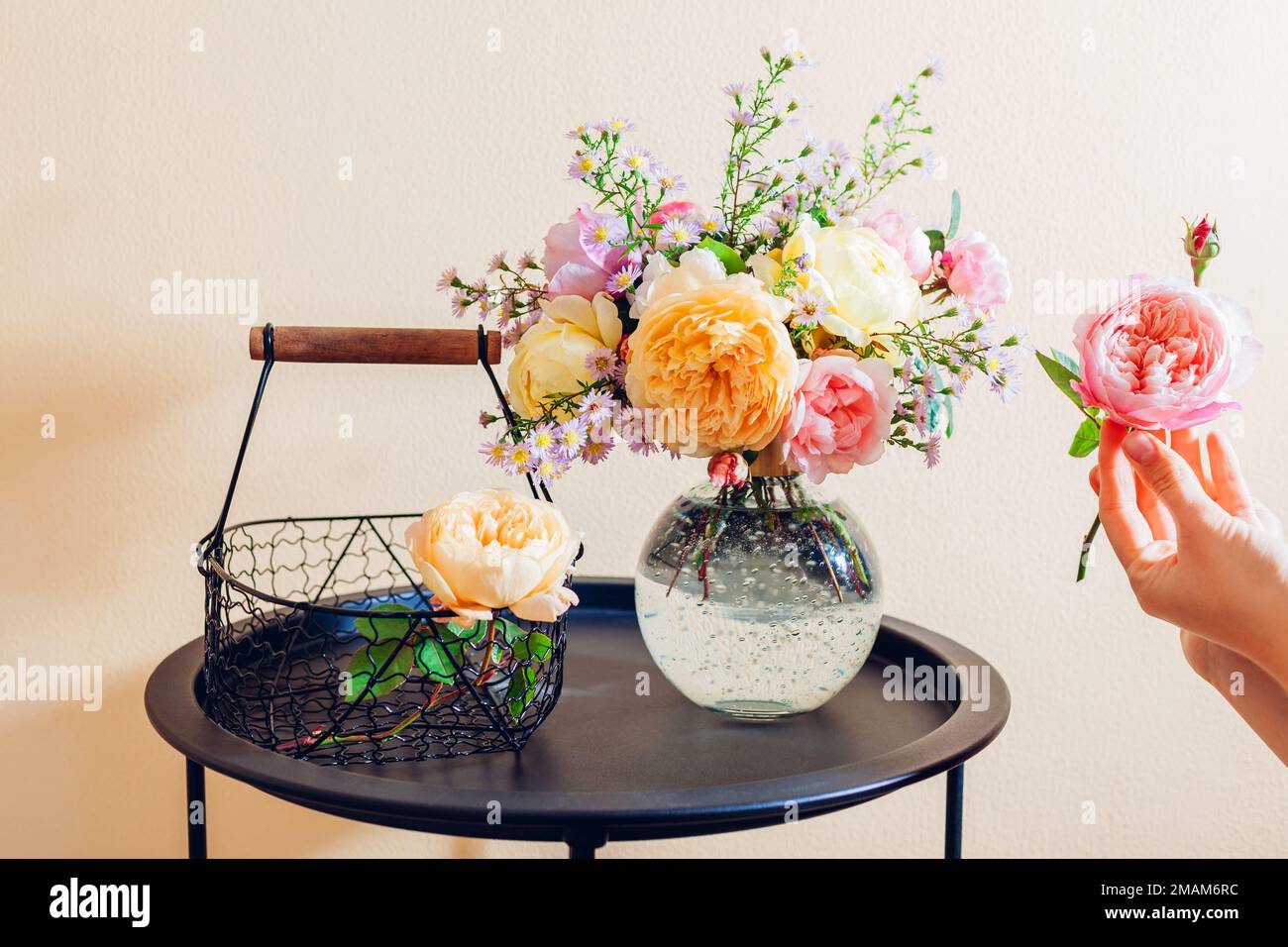 Primo piano di rose inglesi fresche. Donna fa bouquet in vaso trasparente di fiori rosa giallo arancio sul tavolo a casa. Foto Stock