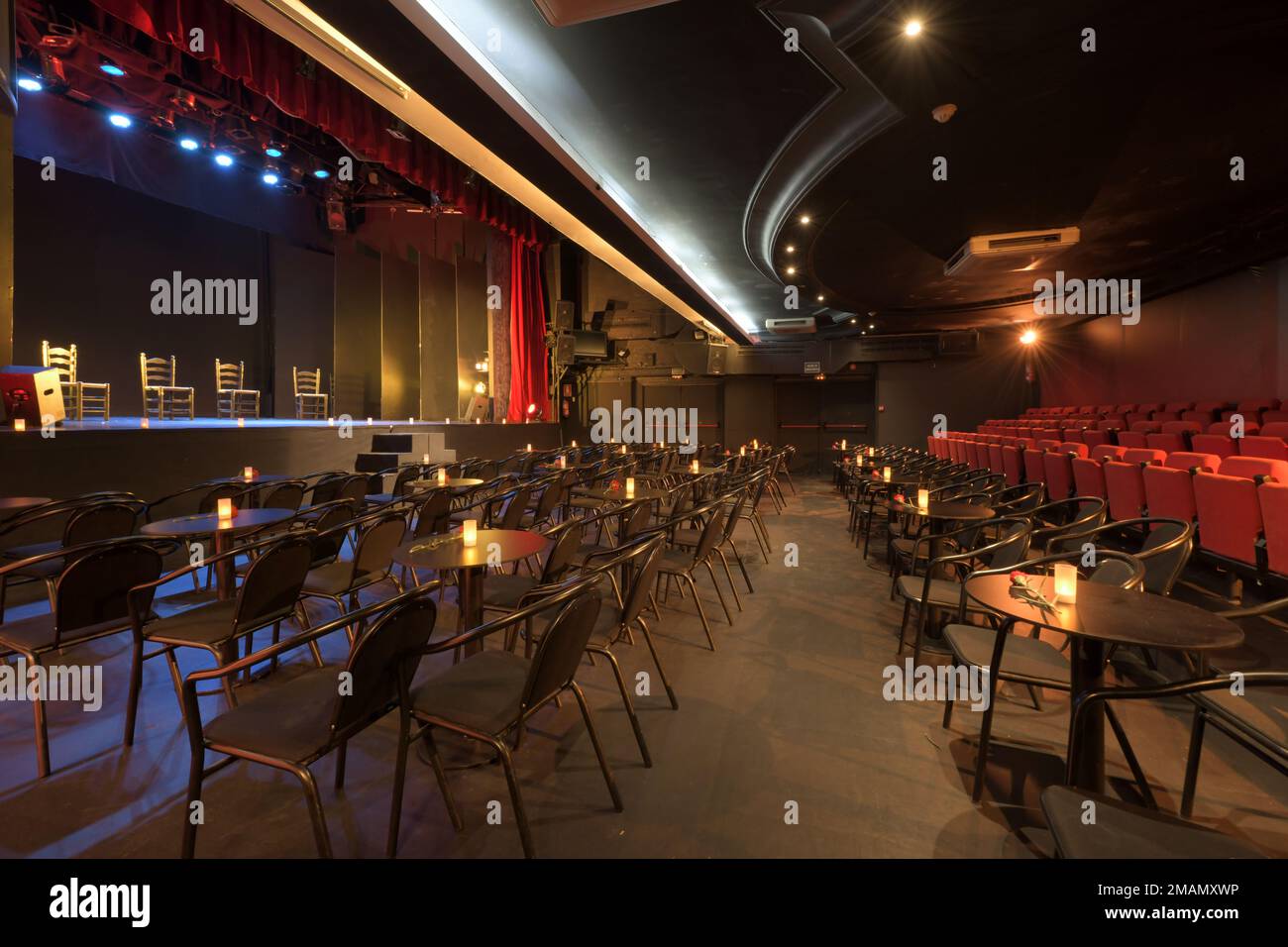 Un teatro vuoto con bancarelle con tavoli e un palco con quattro sedie pieghevoli e sedili in tessuto rosso Foto Stock