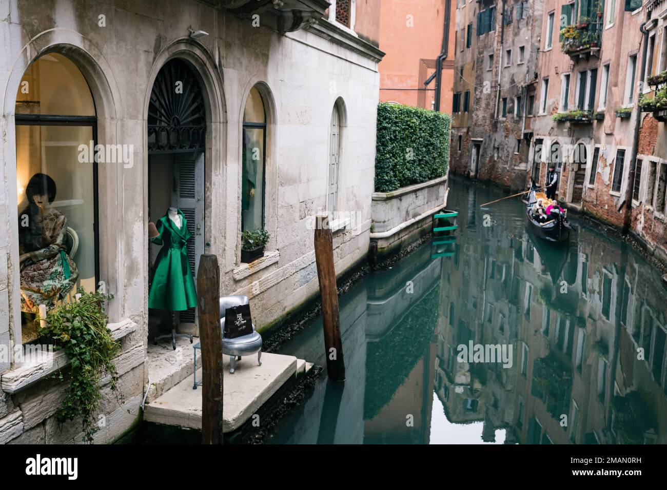 19th gennaio 2023, Venezia Italia. Una gondola si avvicina ad un negozio che presenta un bel vestito verde e manichino su un canale di Venezia. Foto Stock