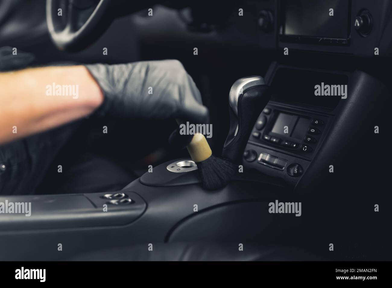 Pulizia della manopola di cambio marcia con spazzola. Mano sfocata nel guanto di gomma protettiva utilizzando una spazzola professionale nel processo di dettaglio dell'auto. Primo piano. Interni di lusso per auto sportive. Foto di alta qualità Foto Stock