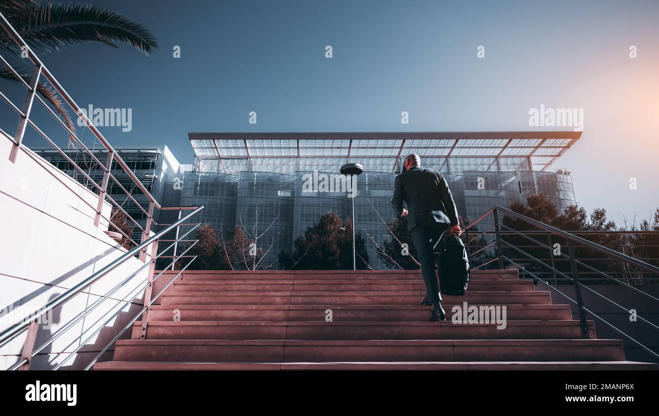 Un sofisticato dirigente africano è stato catturato da dietro camminando su una grande scala verso una m di vetro architettonicamente bella e innovativa Foto Stock