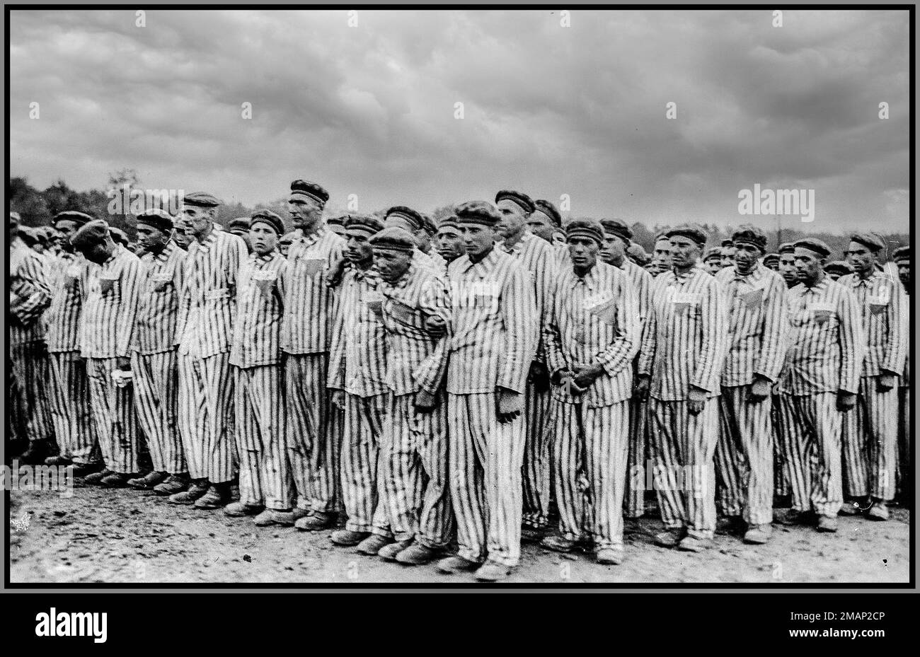 Buchenwald, [Turingia] Germania nazista prigionieri in piedi durante una chiamata. Ciascuno di essi indossa un cappello a righe e un cuscinetto uniforme, con badge triangolari colorati e numeri di identificazione. 1938-1941 Buchenwald Concentation Camp Turingia nazista Germania Foto Stock