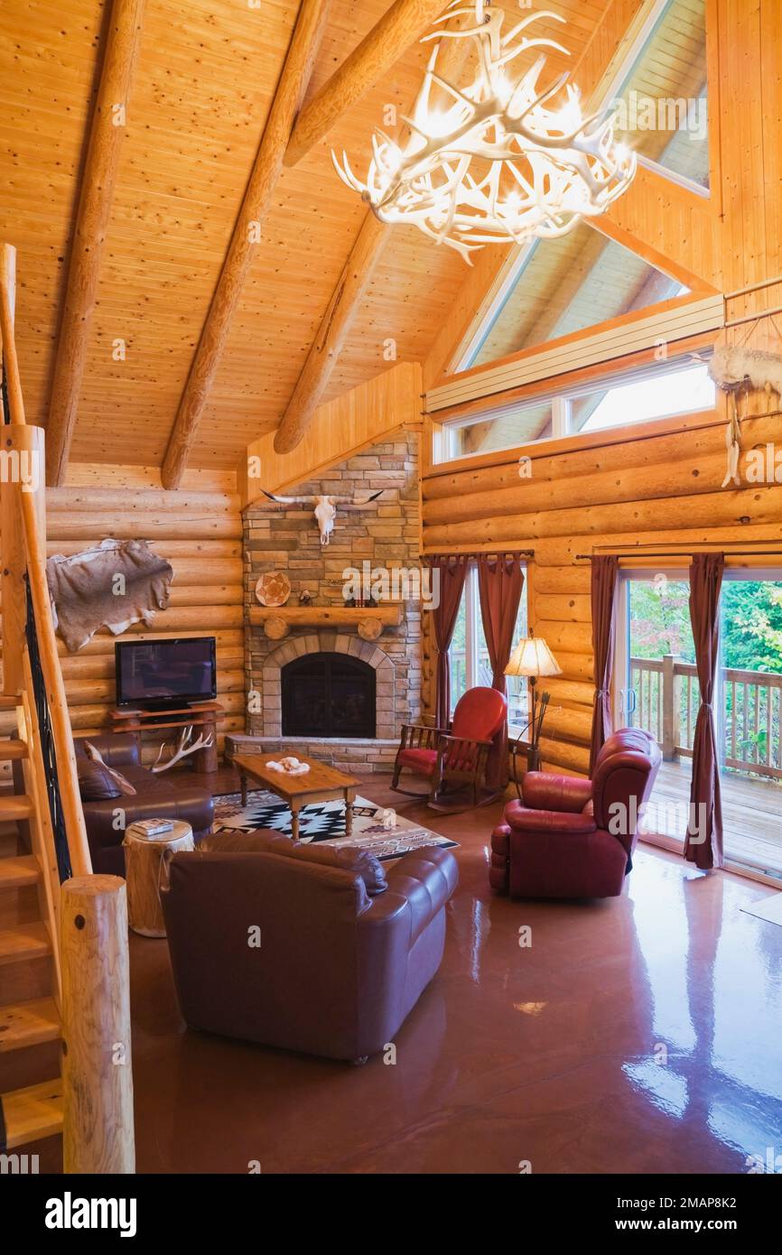 Poltrone in pelle marrone e rossa, caminetto a gas in pietra naturale nel soggiorno all'interno di una casa in legno in stile scandinavo. Foto Stock