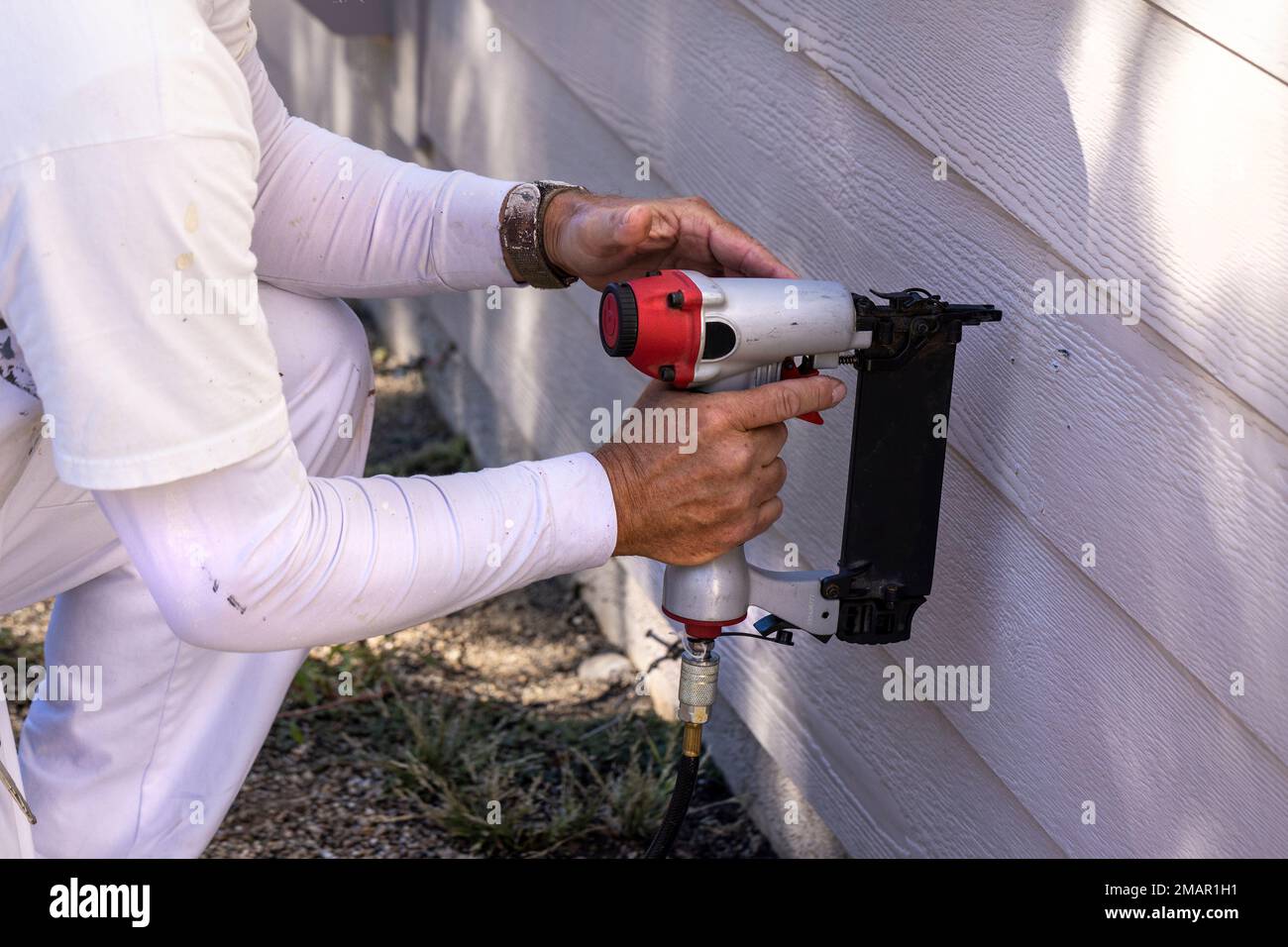 Pittore usando una pistola per unghie per riparare il lato della casa prima di iniziare il lavoro di vernice Foto Stock