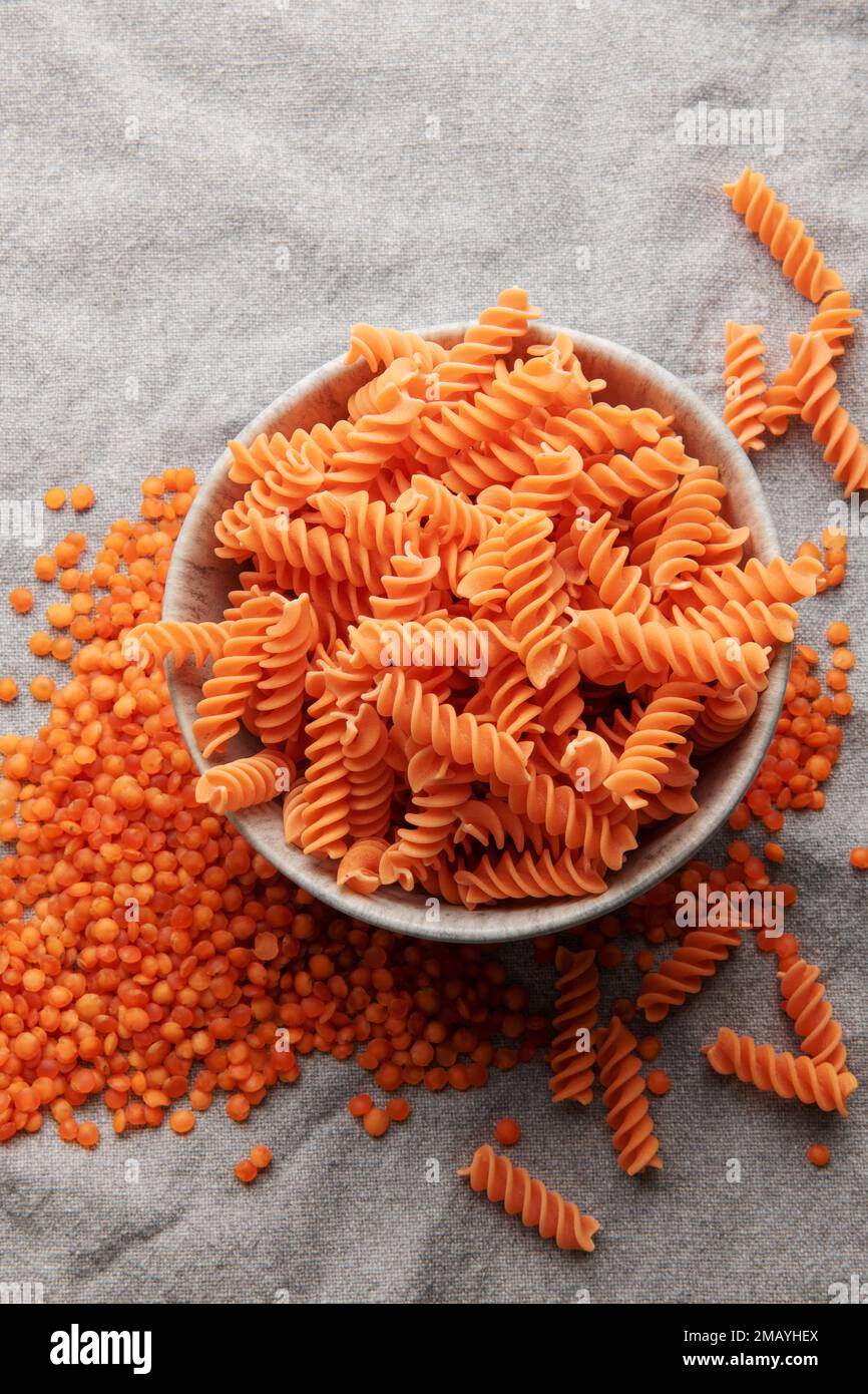 Lenticchie rosse fusilli su fondo tessile grigio. Ciotola con pasta cruda e lenticchie rosse. Pasta senza glutine. Foto Stock